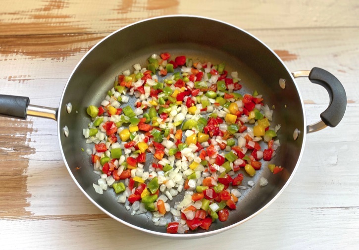Diced onion and bell pepper sautéing in a pan. 