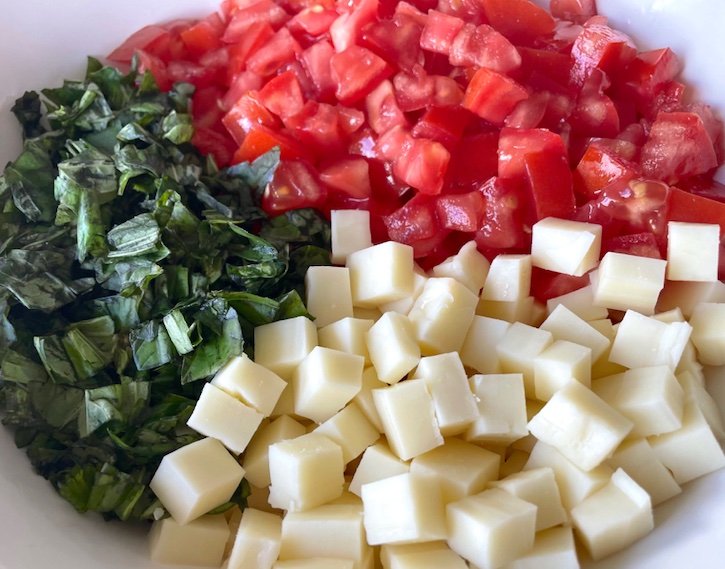 A bowl full of the mixture of chopped mozzarella cheese, tomatoes and fresh basil for making caprese toast. 