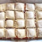 Frozen ravioli in a baking dish with pasta sauce and shredded mozzarella cheese, ready to be baked to make a quick and easy family dinner.