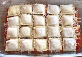 Frozen ravioli in a baking dish with pasta sauce and shredded mozzarella cheese, ready to be baked to make a quick and easy family dinner.