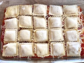 Frozen ravioli in a baking dish with pasta sauce and shredded mozzarella cheese, ready to be baked to make a quick and easy family dinner.