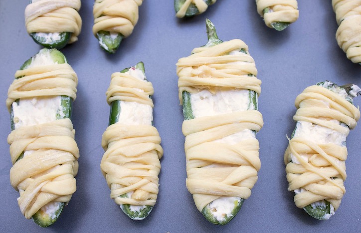 Cream cheese stuffed jalapenos wrapped in refrigerated strips of crescent dough, ready for the oven. 