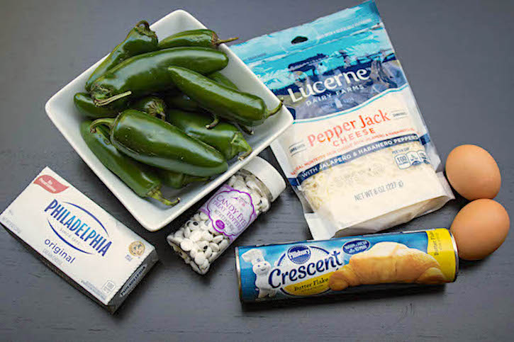 Ingredients to make Jalapeno Popper Mummies including cream cheese, pepper jack cheese, crescent dough, eggs, and candy eyeballs. 