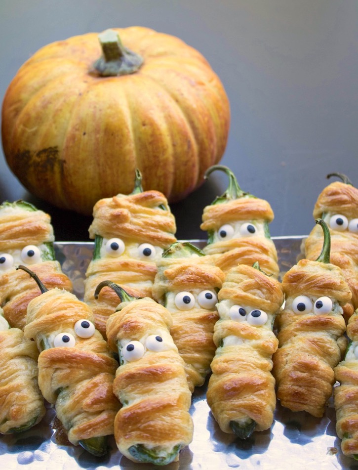 Jalapeño Popper Mummies are a fun and easy Halloween appetizer to make for parties! Simply stuff jalapeño peppers with a cheesy mixture, wrap with strips of crescent dough, and then bake. Don't forget the candy eyes for the finishing touch!