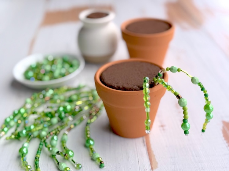 Putting beaded stem wires into a small pot with painted foam to make diy potted plants. 